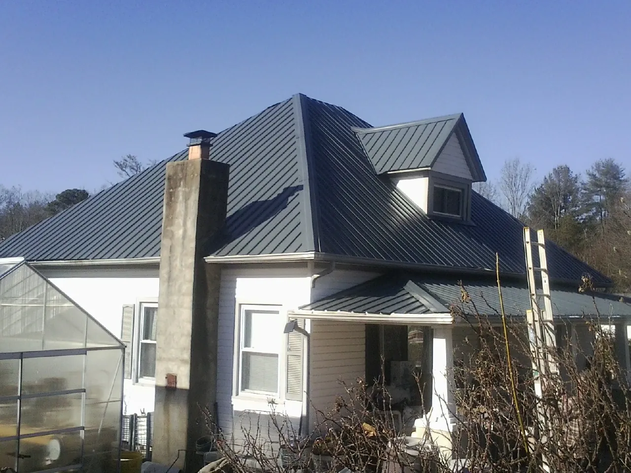 Dark blue standing seam metal roof on a white farmhouse with dormer — Slate & Tile Roof Repair by Roofing Brothers in Watauga