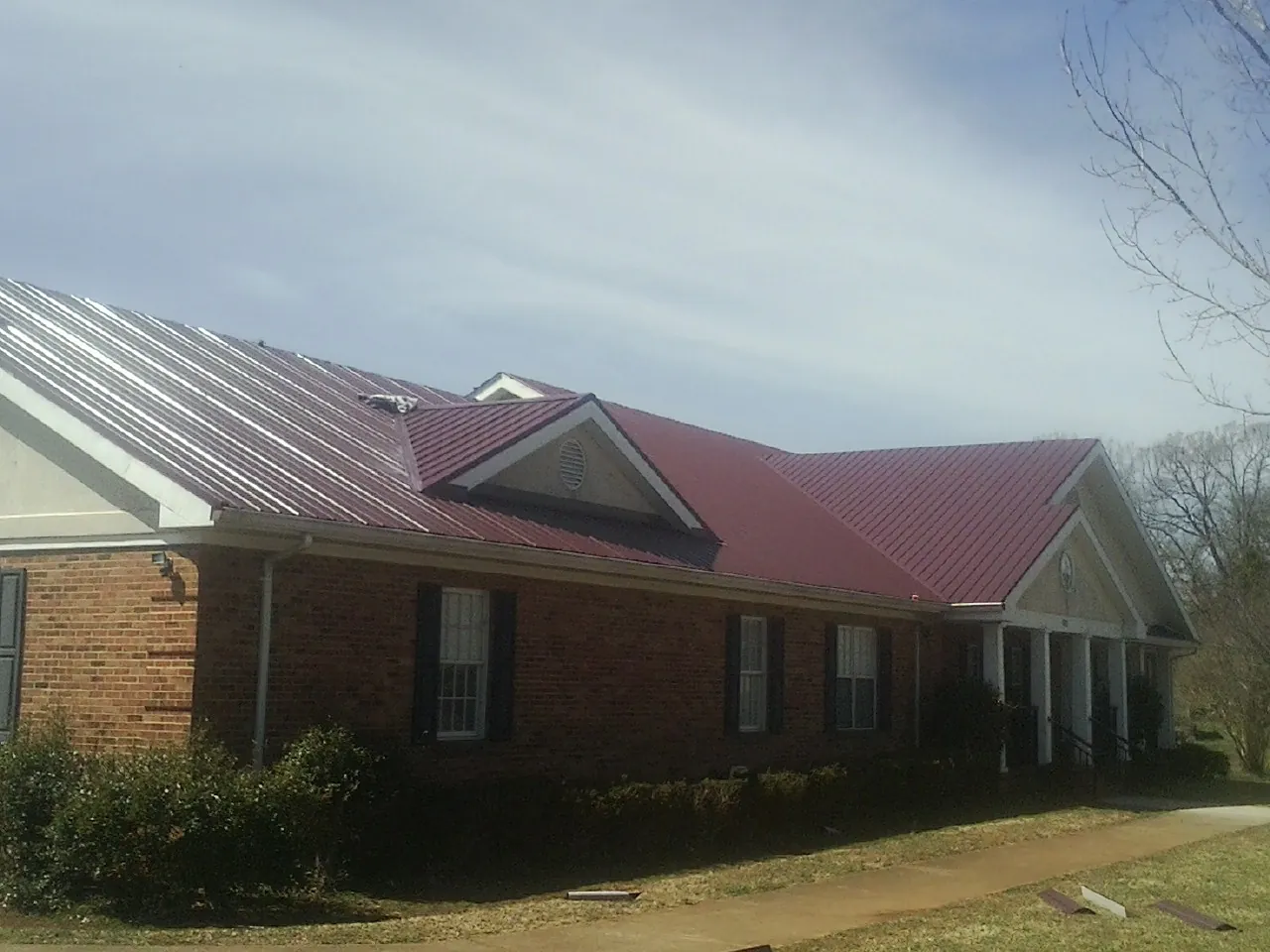 Red metal roof with gabled entries on a long brick building, from a Hail Damage Roof Repair job in Watauga
