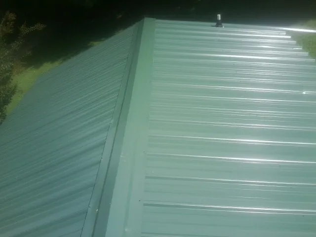 New green metal panels meeting at the ridge of a roof — Flat Roof Repair work by our crew in Watauga