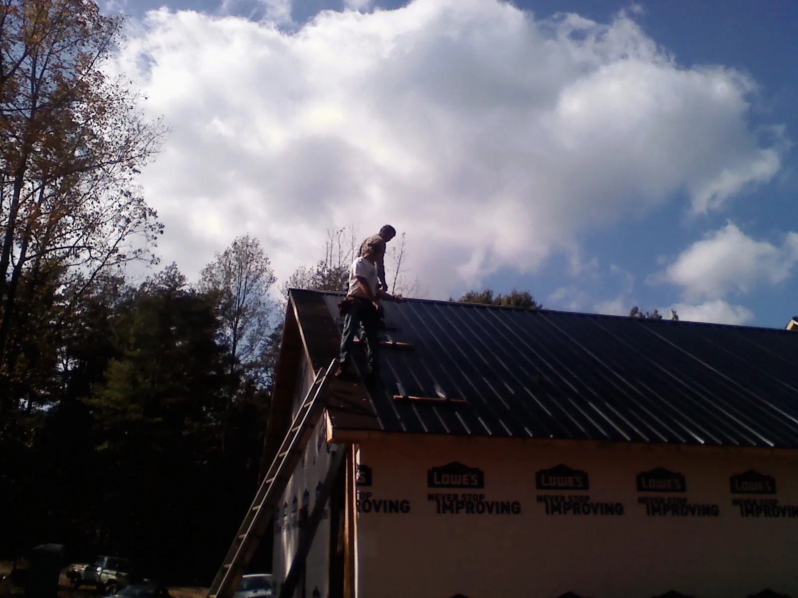 Roofer fastening dark metal panels high against a cloudy sky, from a Roof Inspection job in Watauga