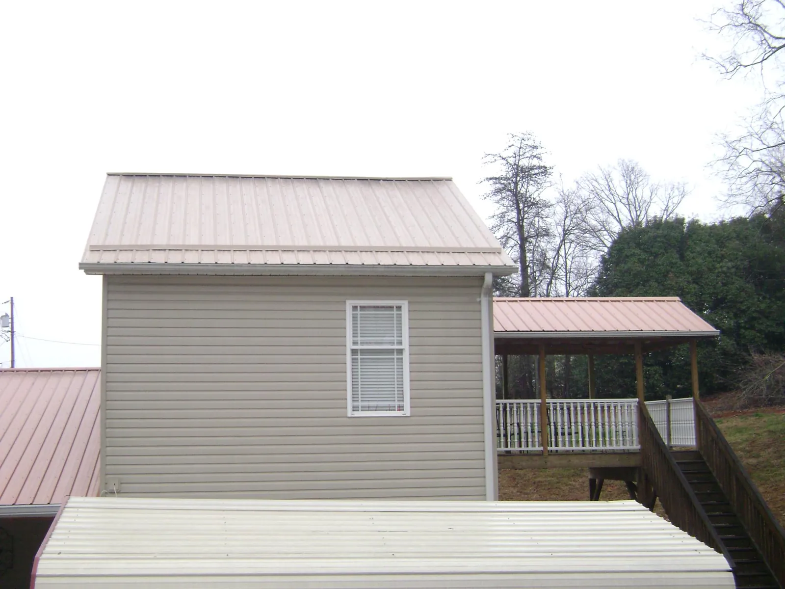 Tan metal roofs on a two story addition and attached porch, from a Roof Replacement job in Watauga